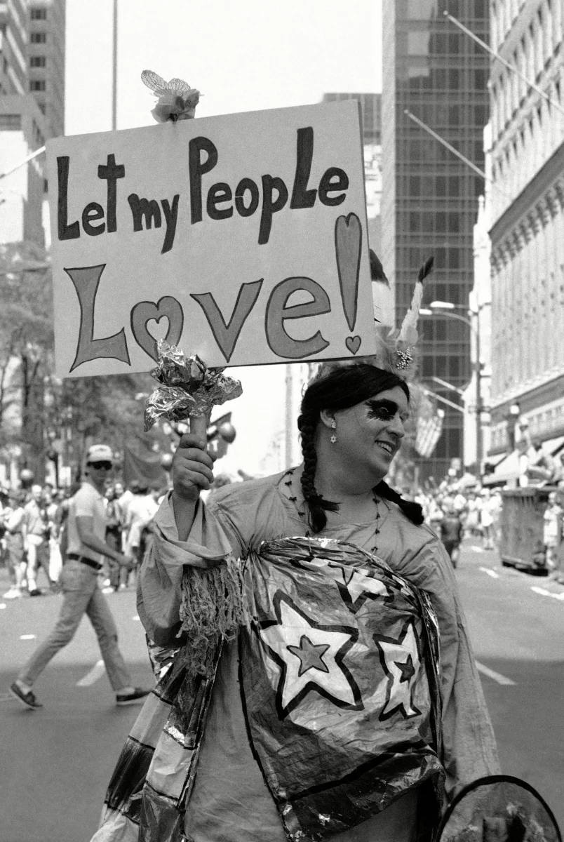 pride month sign let my people love being held by man in parade