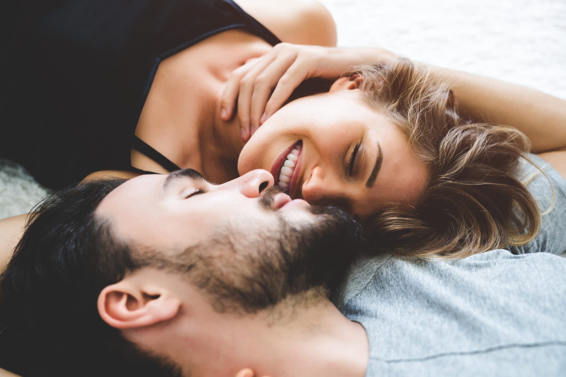 close-up of a woman and a man looking at each other's faces while lying on a bed, talking about using a massage oil