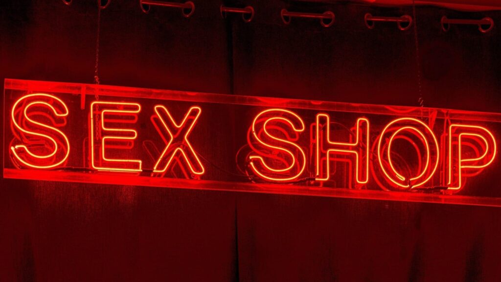 Red neon “SEX SHOP” sign representing a traditional adult store