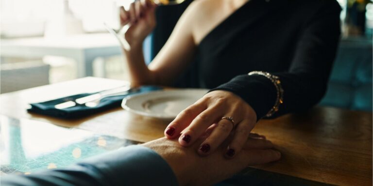 A quiet romantic moment as two people share gentle touch across a table during an intimate date