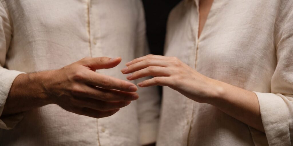 Aphrodisiac oils represented through a quiet moment of intimacy, with two people standing close and hands gently reaching toward one another