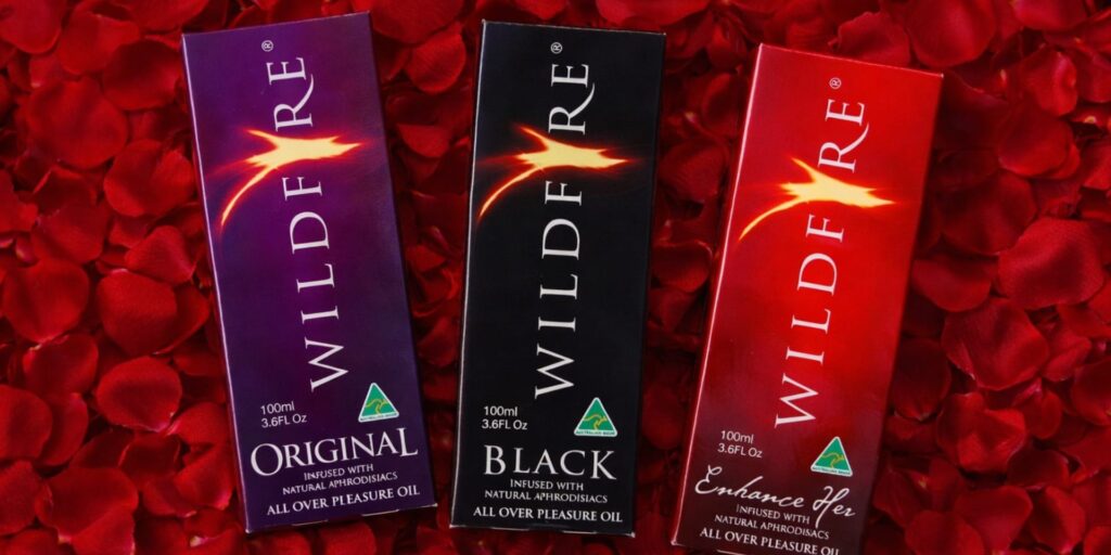 Wildfire massage oil displayed on red rose petals, featuring Original, Black and Enhance Her oils for connection and care