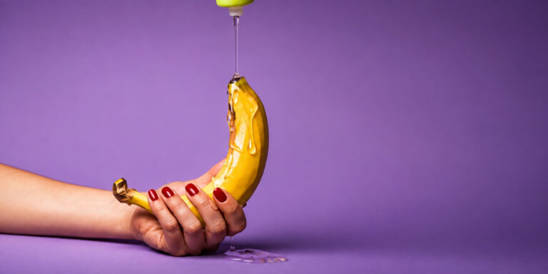 Hand holding a banana with oil drizzling over it, illustrating lube alternatives