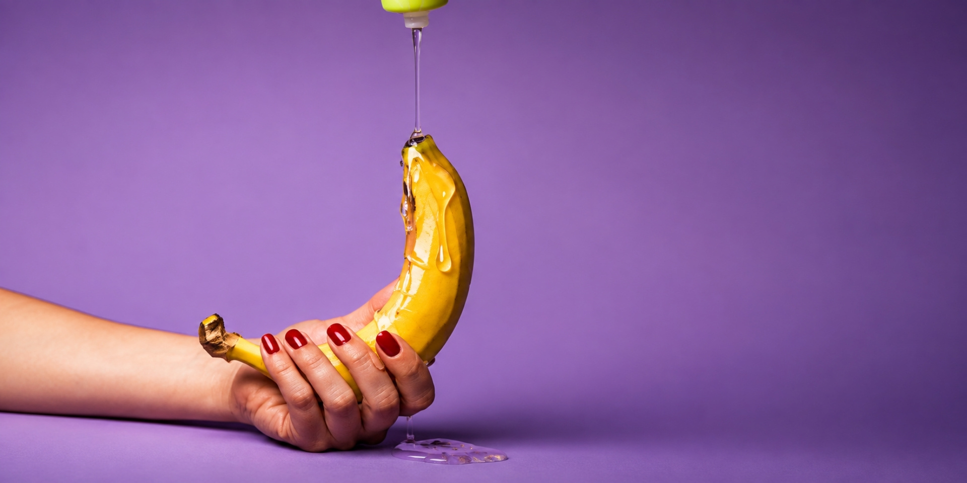 Hand holding a banana with oil drizzling over it, illustrating lube alternatives